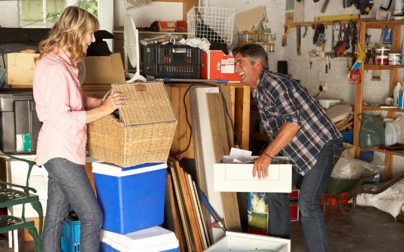 a women holding a junk basket and a man holding a storage with junks that is ready for cleaning out from their garage, both smiling