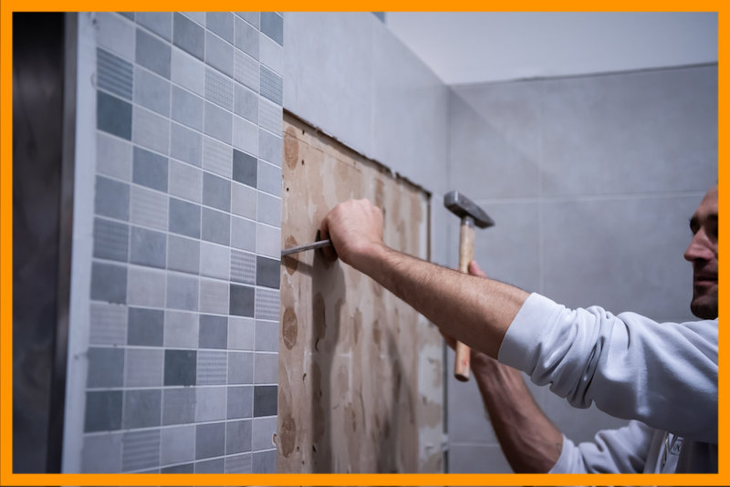 Professional worker remove demolish old tiles in a bathroom with hammer and chisel.