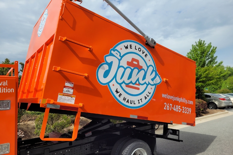 We Love Junk orange truck for hauling and other junk removal services parked beside the road