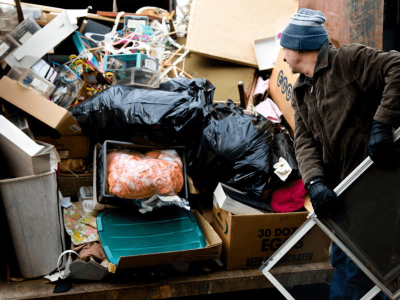 Man removing furniture and household junk from a cluttered dumpster