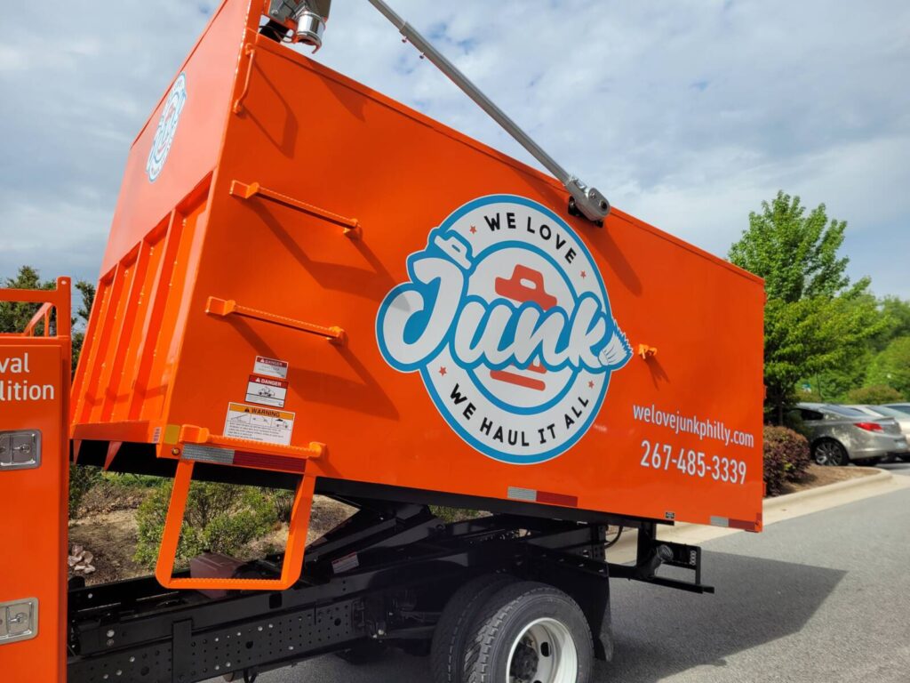 Bright orange We Love Junk truck with company logo