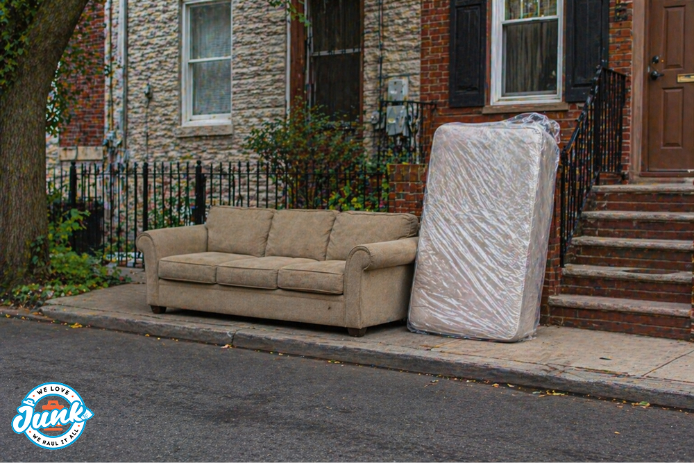Sofa and plastic-wrapped mattress set on the sidewalk outside a brick rowhouse for bulk trash pickup